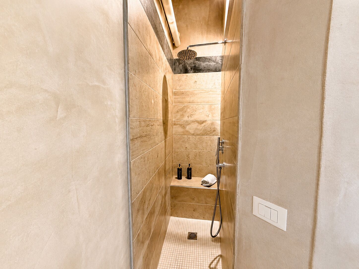 Een kleine douchecabine met een handdouche, een handdoekhouder en een plank met toiletartikelen.