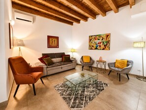 Una sala de estar con un sofá, sillones, una mesa de centro de vidrio y una alfombra estampada.
