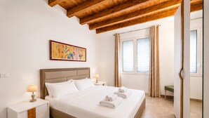 Habitació d'hotel amb llit, taules de nit, un quadre, una finestra amb cortines i sostre de fusta.
