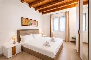 Habitación de hotel con cama, mesitas de noche, un cuadro, ventana con cortinas y techo de madera.