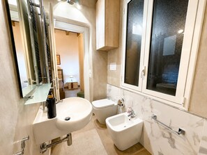 Un baño moderno con un espejo grande, un lavamanos, un bidé y una ventana.