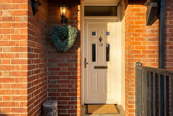 A brick exterior with a white door marked '19' and a wreath above it.