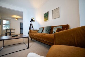 En stue med sofa, sofabord og gulvlampe. Et vindue og en dør er synlige i baggrunden.
