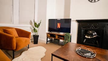 Ein Wohnzimmer mit einer Couch, einem Couchtisch, einem Fernseher, einem Kamin und einer Wanduhr.