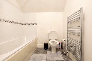 Et badeværelse med badekar, toilet og håndklædetørrestativ.