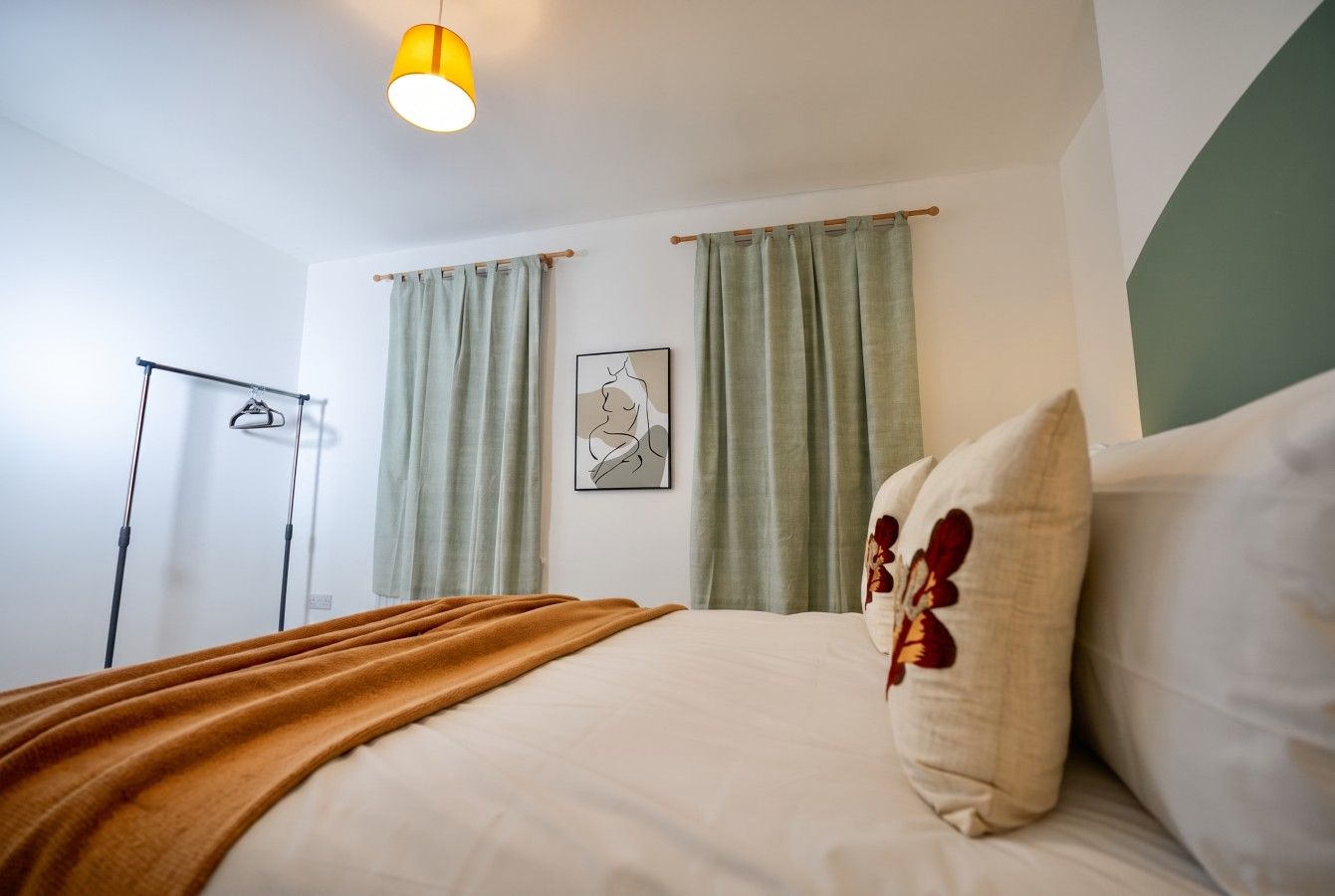 A hotel room with a bed, a bedside lamp, a wall-mounted artwork, and a clothing rack.