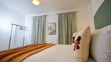 A hotel room with a bed, a bedside lamp, a wall-mounted artwork, and a clothing rack.