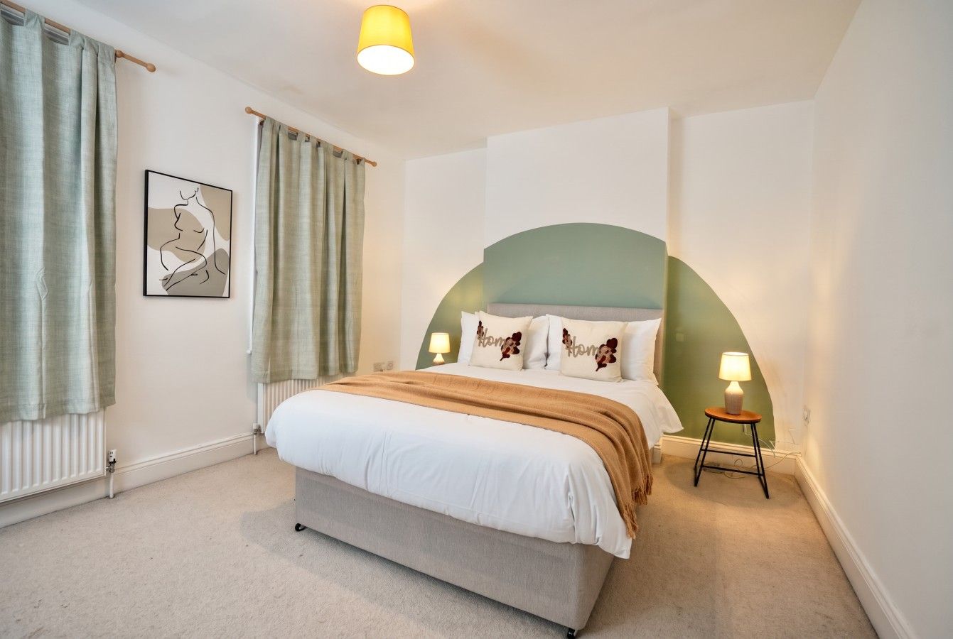 Ein Schlafzimmer mit Bett, Nachttisch, Lampe, Heizkörper und einem Wandbild.