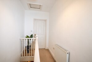 A narrow hallway with a white door at the end, a white radiator on the right, and a white railing in the foreground.