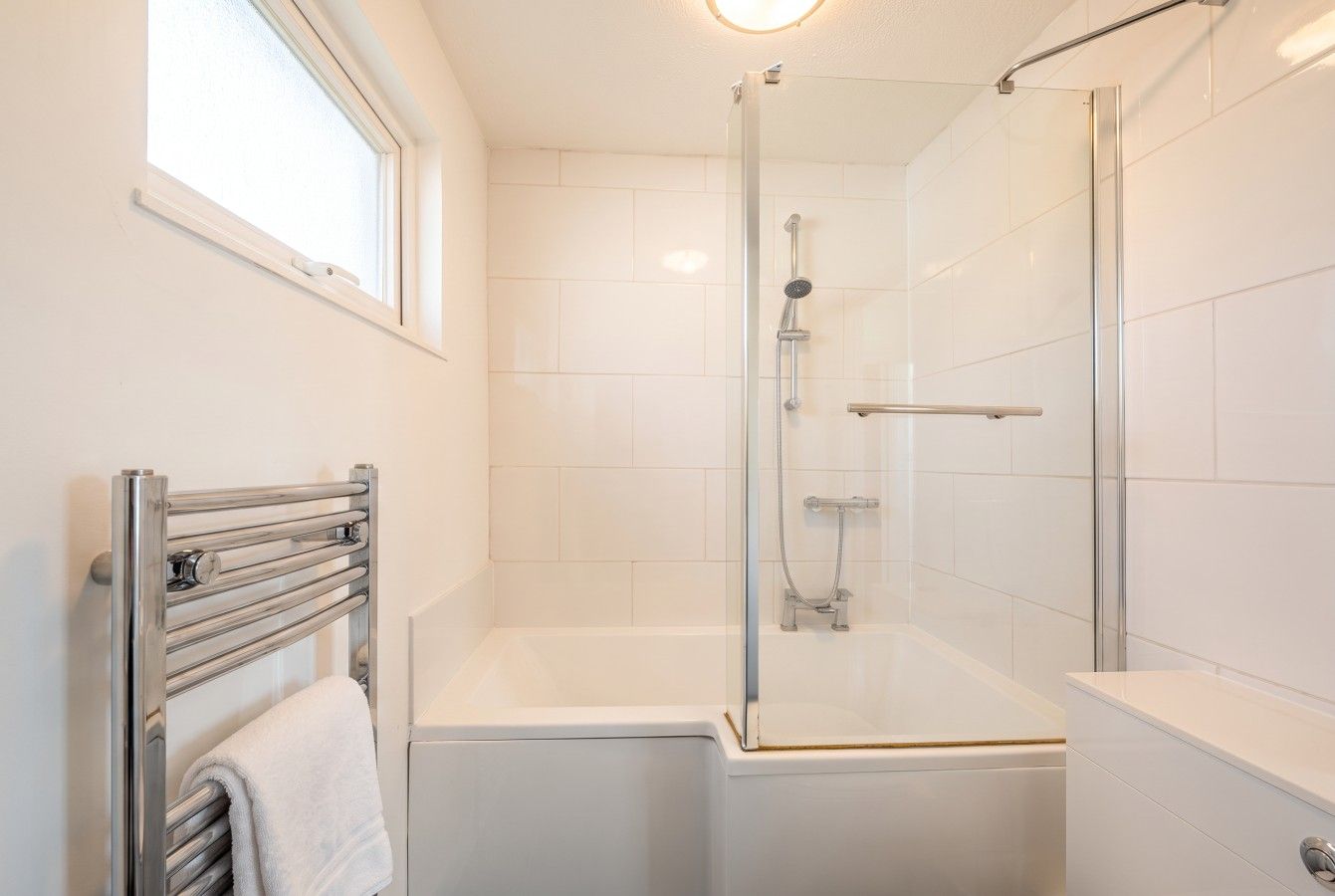 A modern bathroom with a glass-enclosed shower, a white bathtub, and a towel rack.