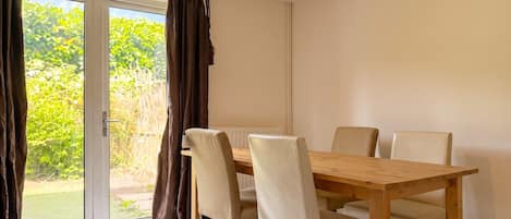 A dining area with a wooden table and chairs, a sliding glass door to the outdoors, and a ceiling light fixture.