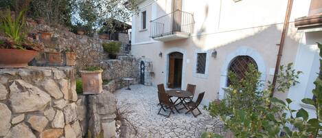 A courtyard with stone walls, a table and chairs, and potted plants.