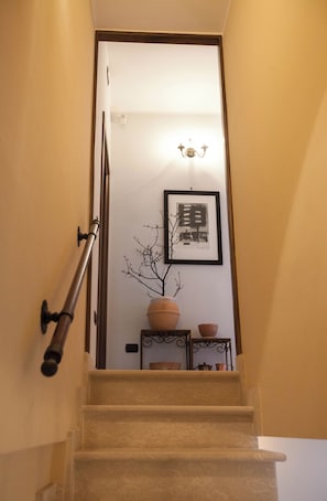 Eine Treppe führt zu einem Raum mit einem gerahmten Kunstwerk, einer Vase und einem kleinen Tisch.