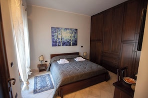 Ein Schlafzimmer mit Bett, Nachttisch, Lampe, einem Gemälde, einem Kleiderschrank und einer Tür.