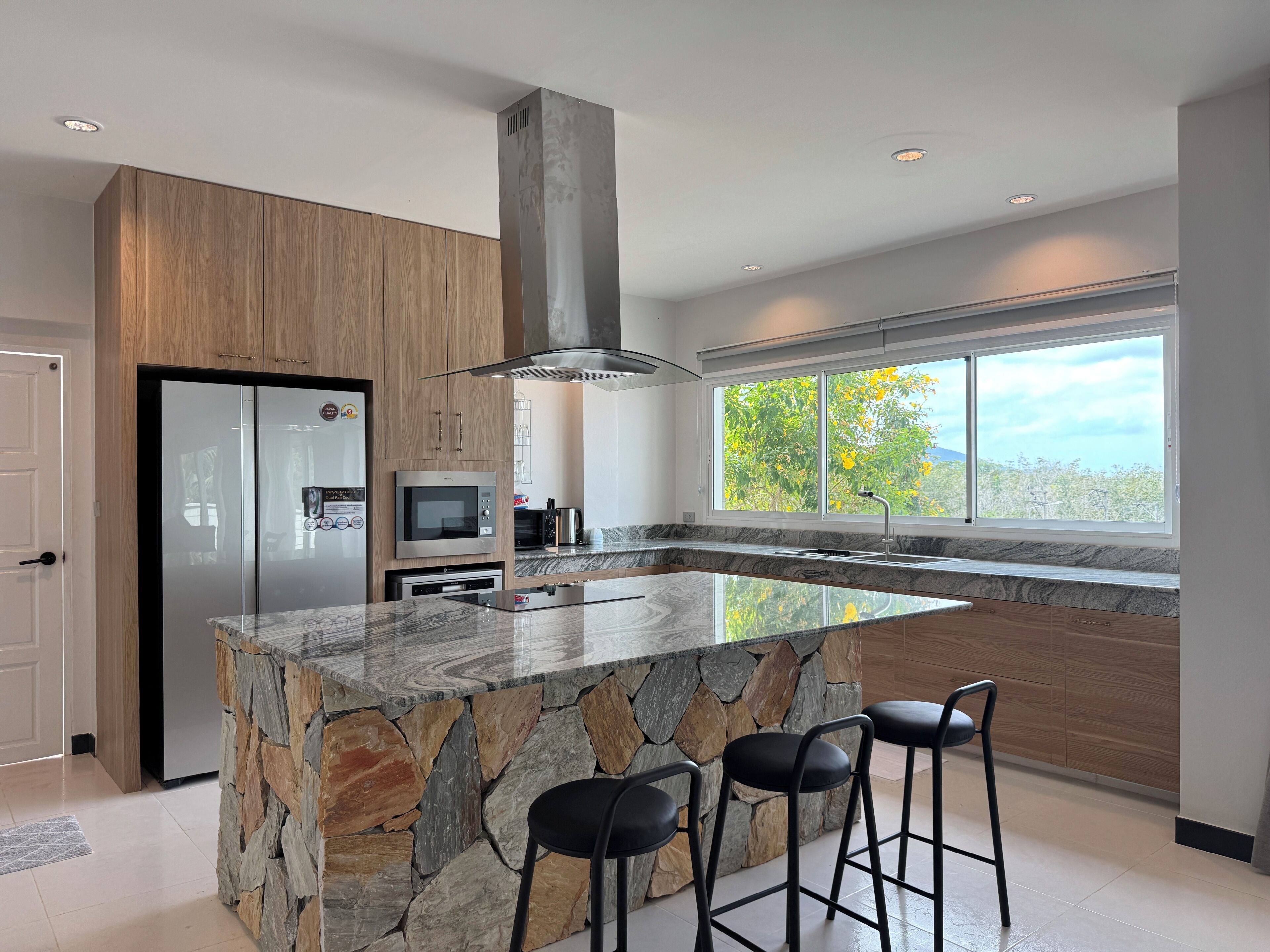 A modern kitchen with a large island, built-in appliances, and a view of trees through the window.