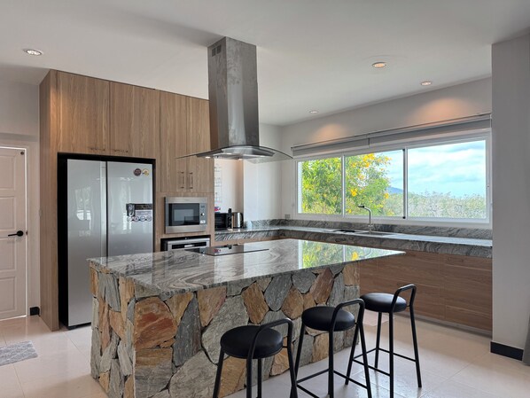 A modern kitchen with a large island, built-in appliances, and a view of trees through the window.