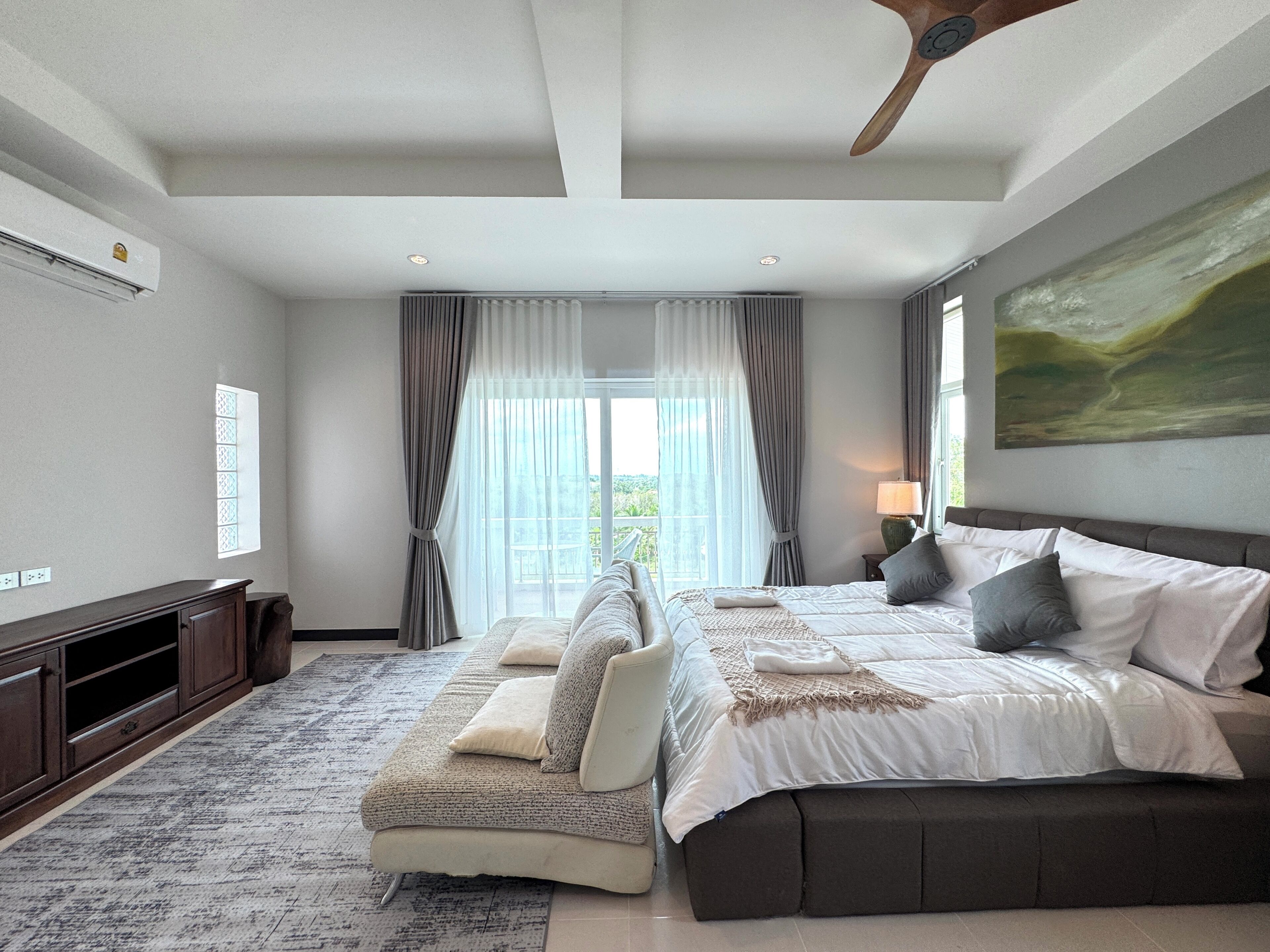 A modern bedroom with a large bed, a sofa, a TV, and a ceiling fan.