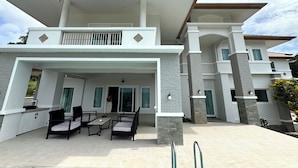Uma casa moderna de dois andares com um alpendre coberto, móveis de exterior e uma escadaria visível que leva ao andar superior.