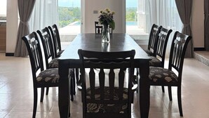 Uma sala de jantar com uma mesa retangular, seis cadeiras, um lustre e um vaso com flores.