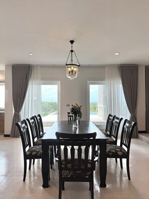 A dining area with a rectangular table, six chairs, a chandelier, and a vase with flowers. - Panoramic Sunset View Private Pool Villa, Maikhao beach (Thalang)
