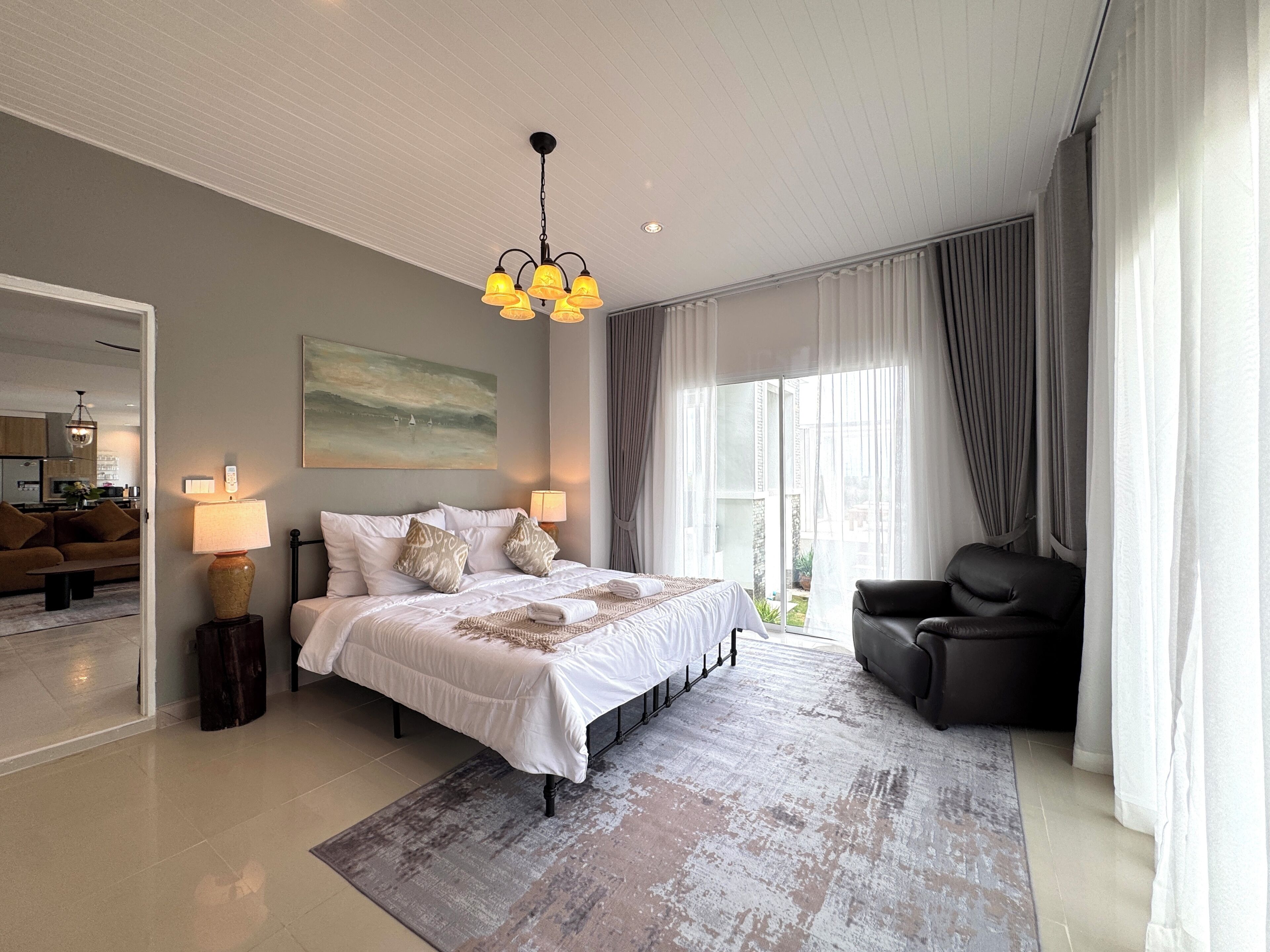 A spacious bedroom with a large bed, a sitting area with a chair, and a view of the outdoors.