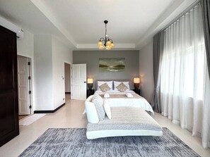 A hotel room with a bed, a nightstand, a lamp, a painting on the wall, and a view of the outdoors through the window. - Panoramic Sunset View Private Pool Villa, Maikhao beach (Thalang)