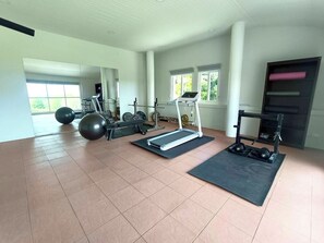 A gym with exercise equipment, large windows, and a tiled floor.