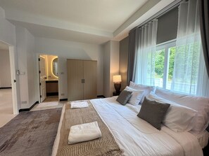 Ein Hotelzimmer mit einem großen Bett, einem Kleiderschrank, einem Badezimmer und Blick auf Grünfläche.