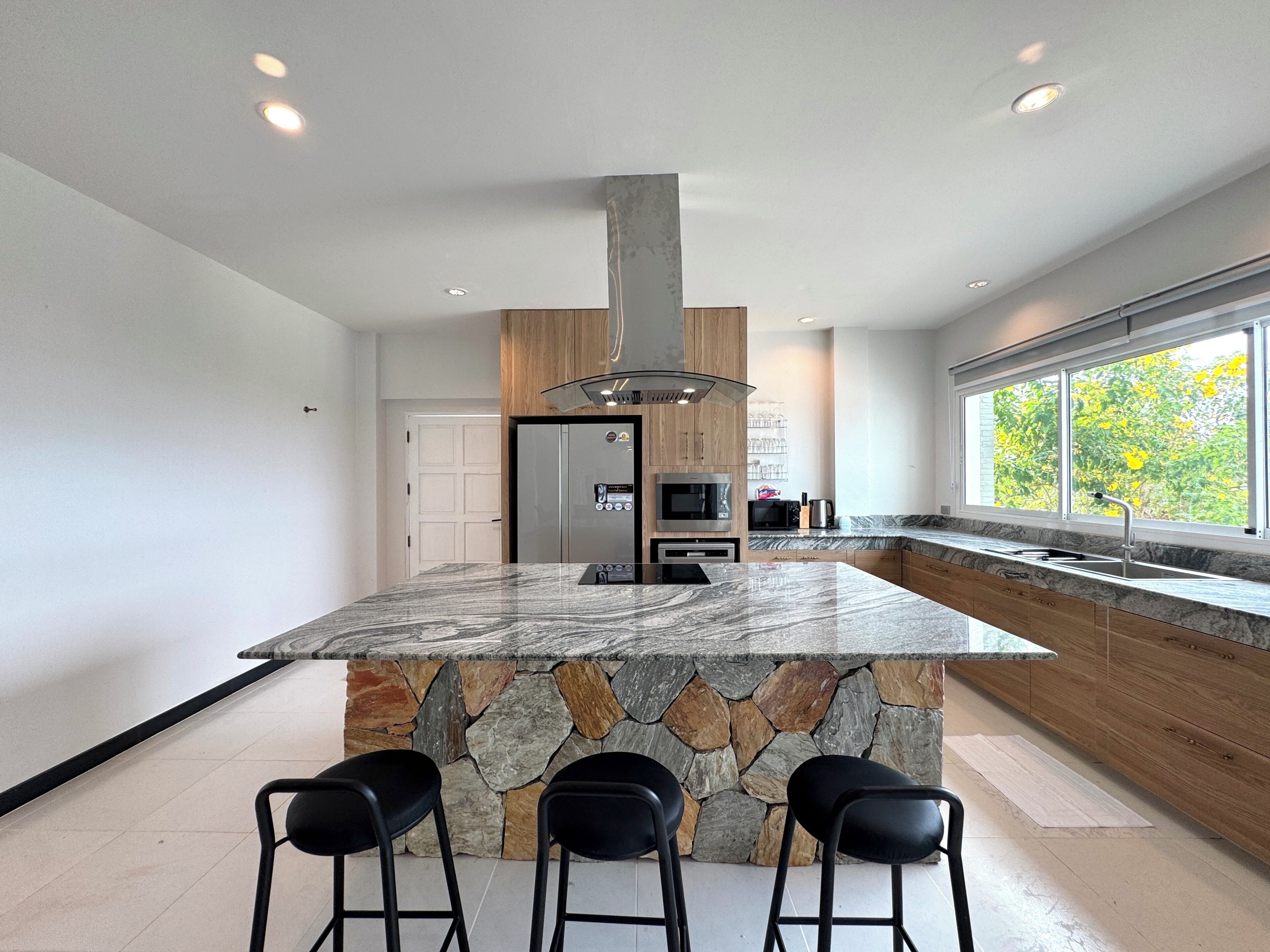 A modern kitchen with a central island, built-in appliances, and a large window.