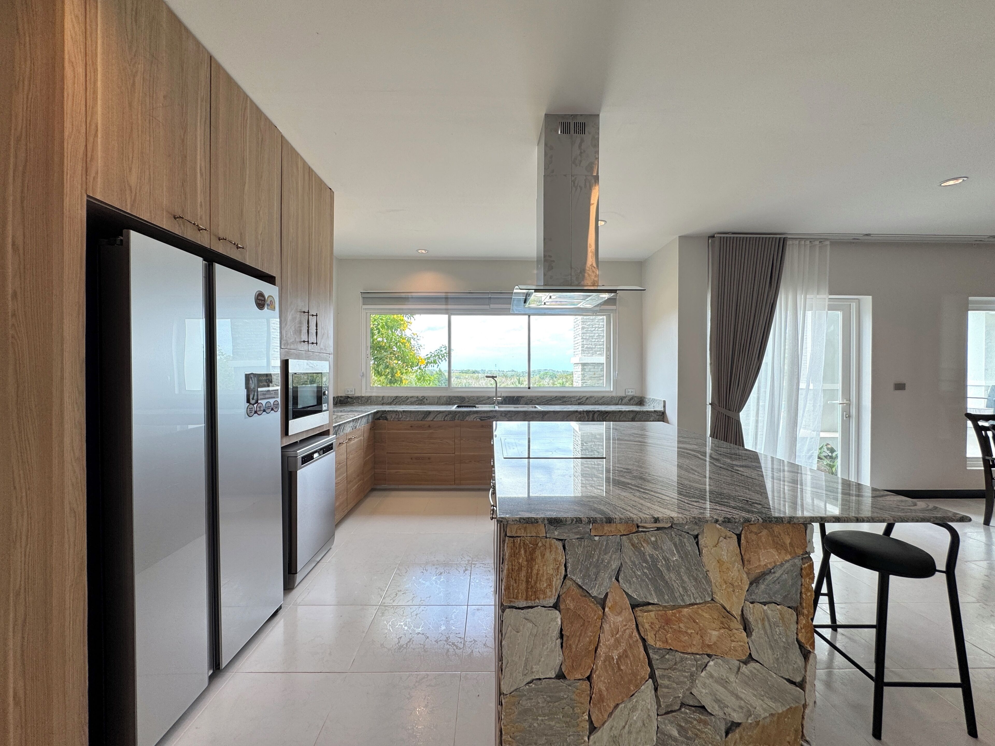 A modern kitchen with a stone island, built-in appliances, and a view to the outdoors.