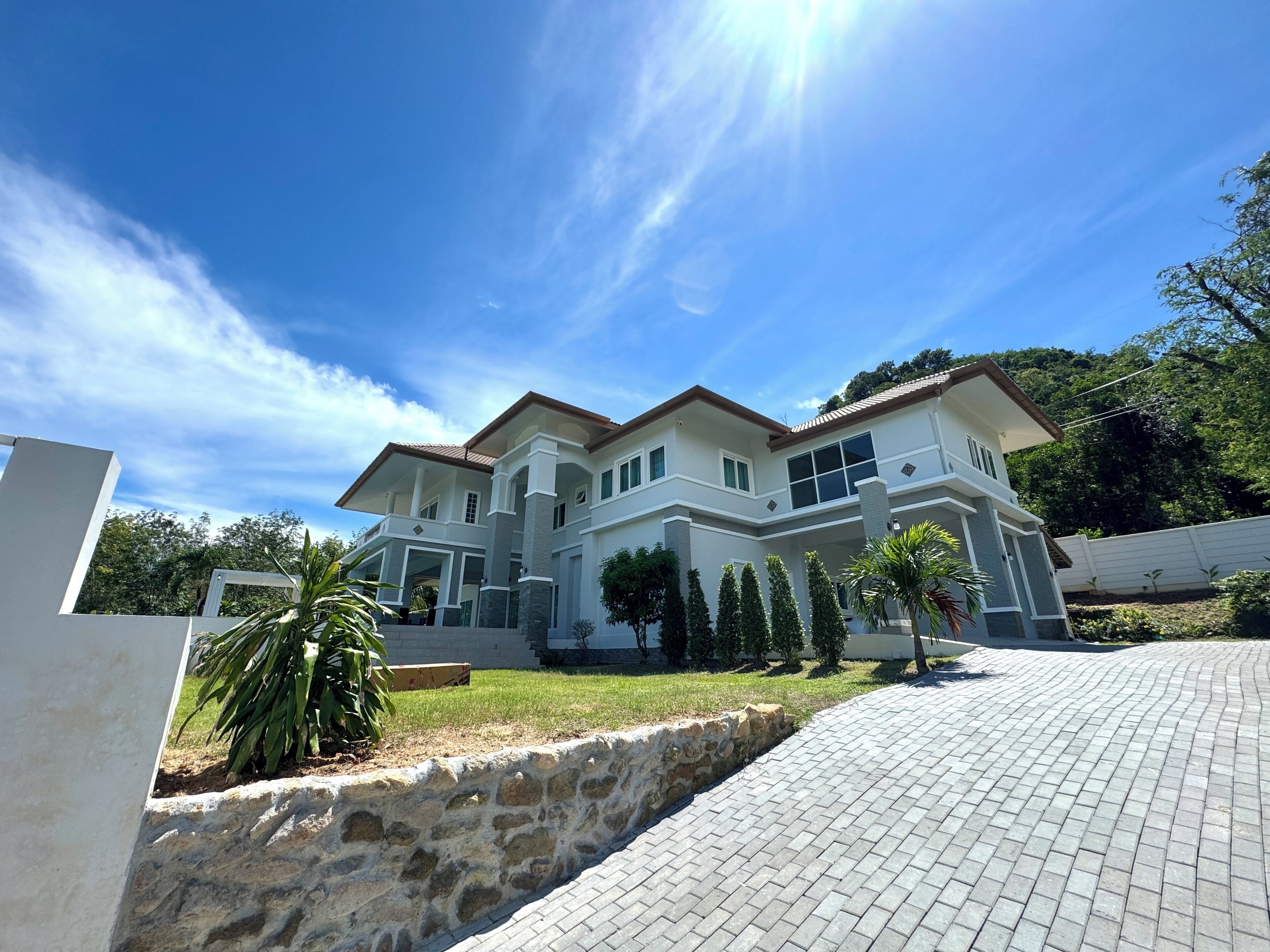 A two-story house with a stone retaining wall and a paved driveway.