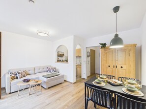 A modern living space with a sofa, coffee table, dining table set for four, and a kitchen in the background.