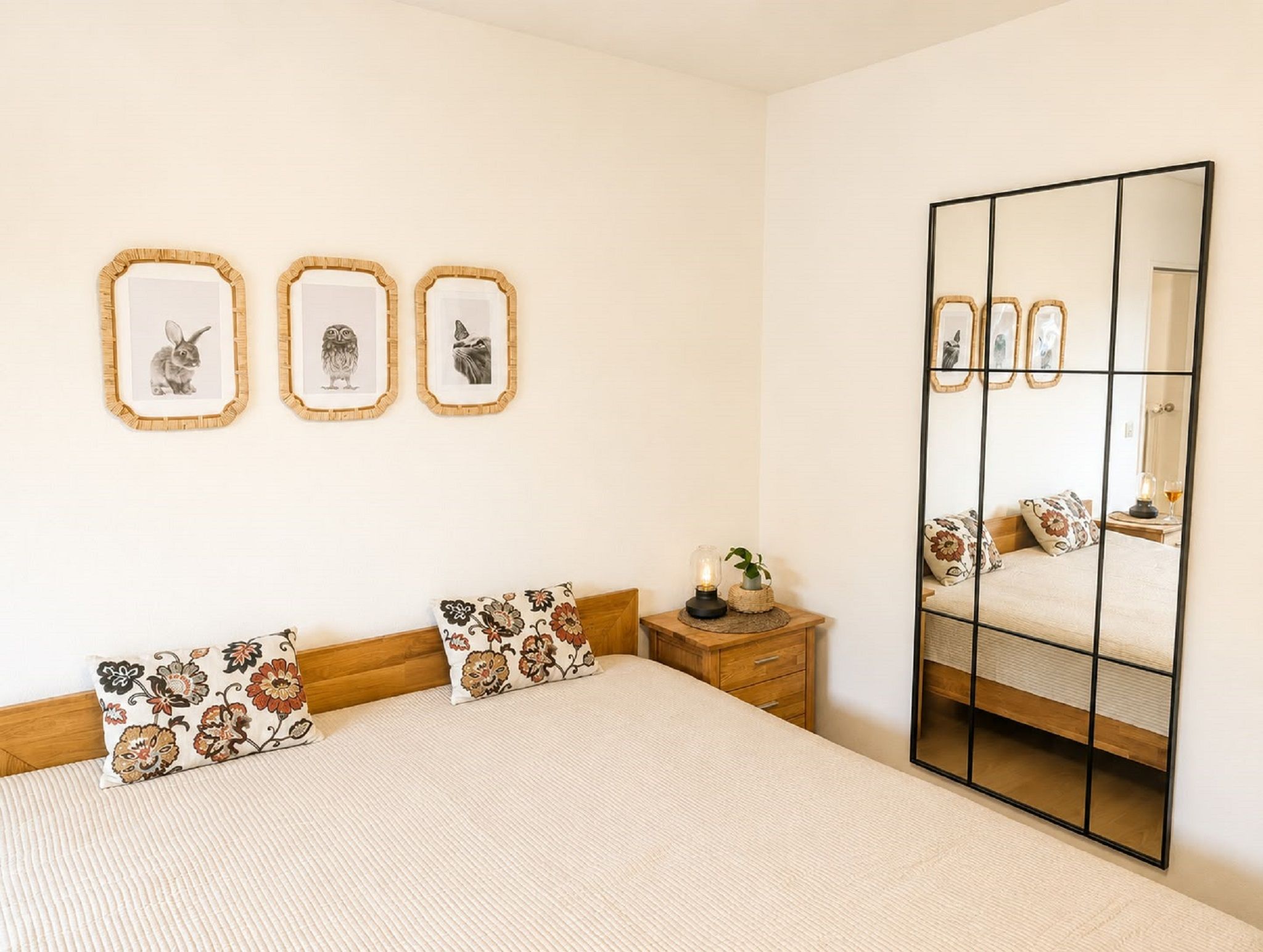 Una camera da letto con un letto, due cuscini, un comodino, uno specchio e tre quadri appesi al muro.