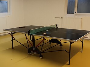 A table tennis table with wheels, positioned in a room with yellow flooring and white walls.