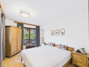A bedroom with a large bed, wooden wardrobe, and a balcony with wicker chairs.