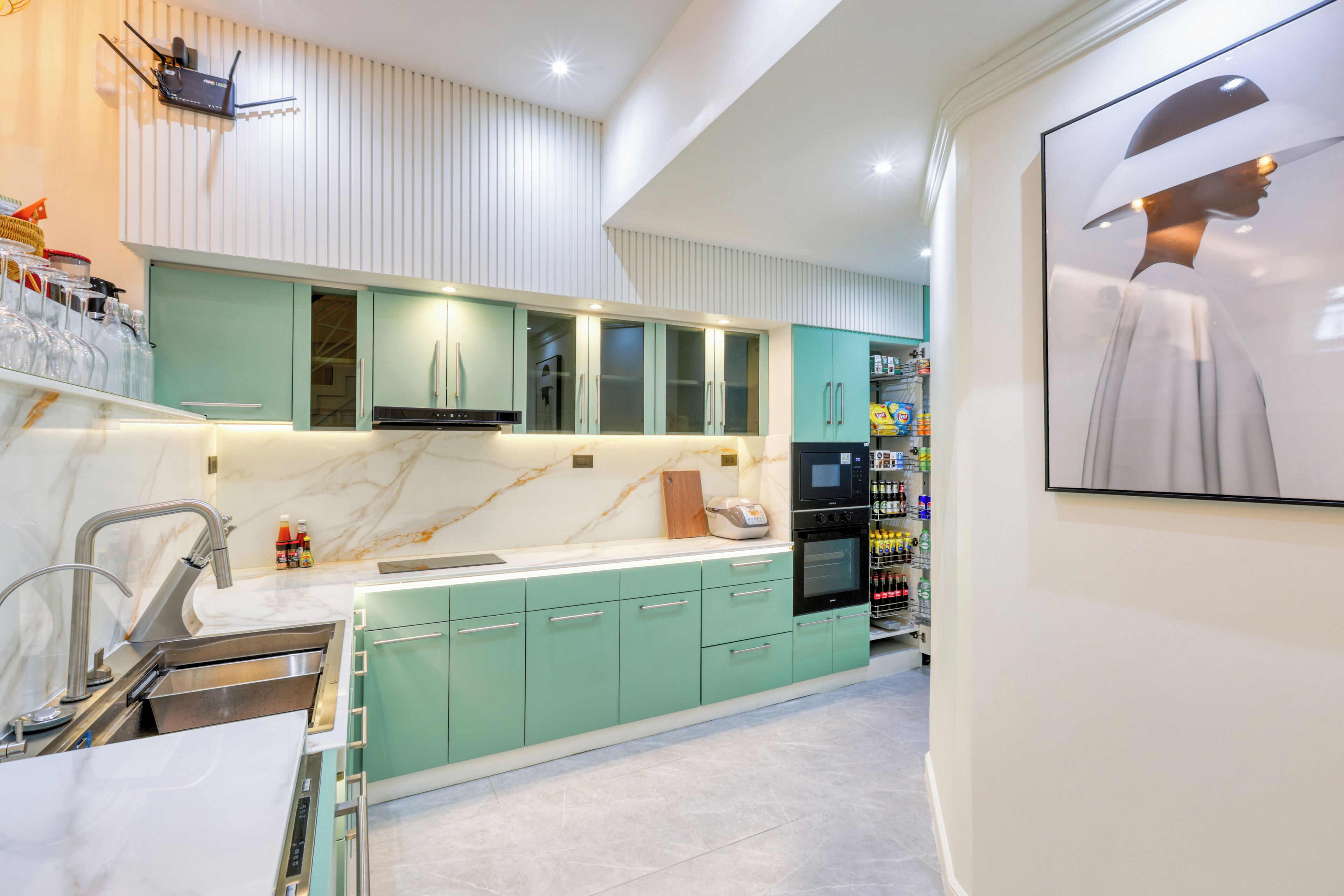 Una cocina moderna con armarios azul verdoso, encimera de mármol y horno empotrado.