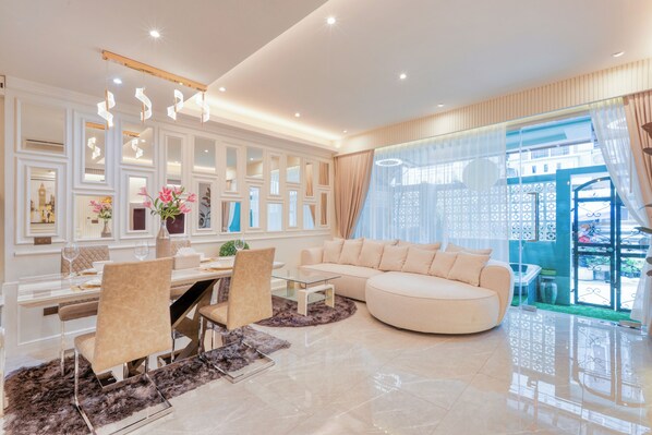 Una sala de estar moderna con una mesa de comedor de vidrio, sofás color beige y un amplio ventanal con cortinas.