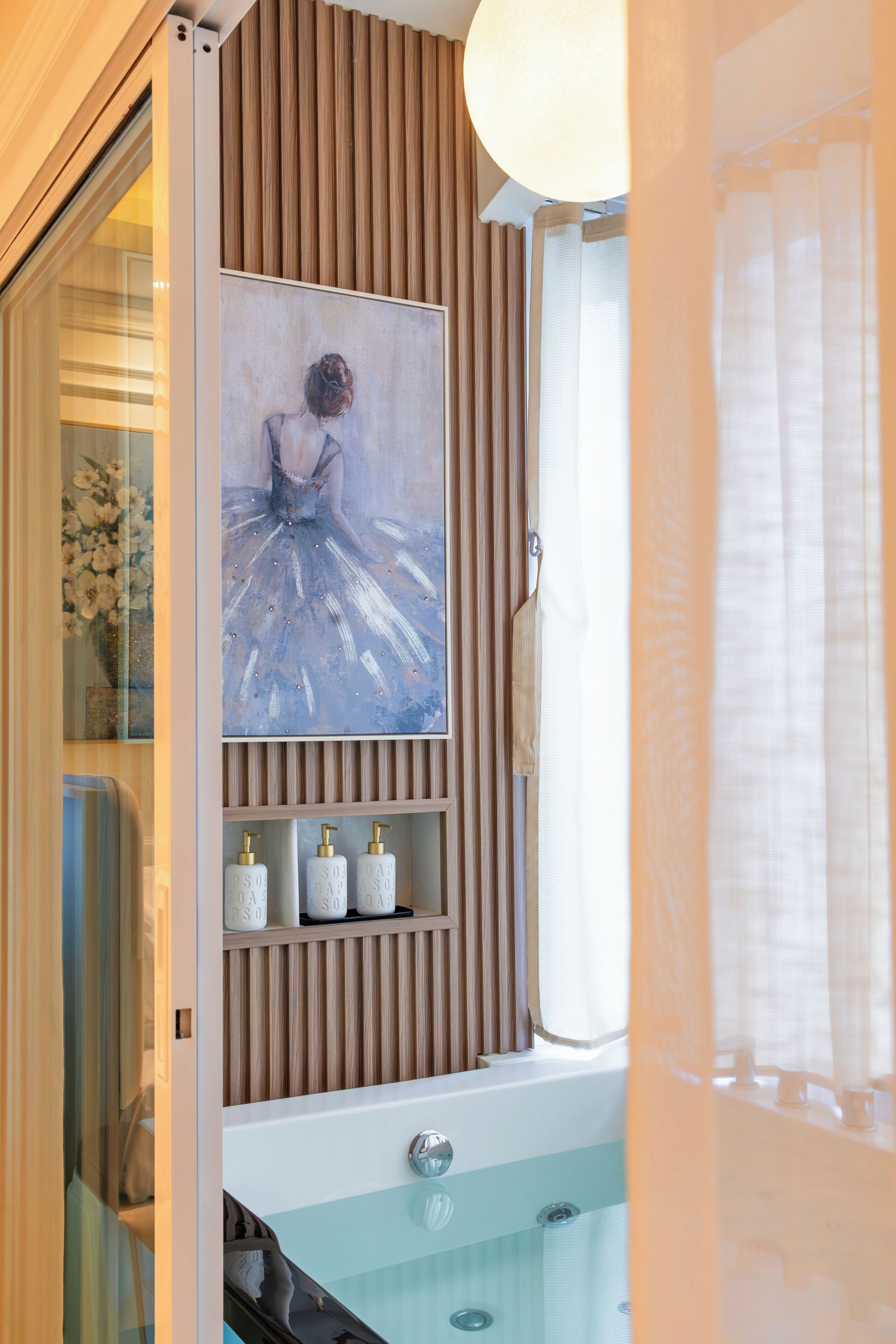 Un baño con una bañera, un cuadro de una bailarina y tres dispensadores de jabón en un estante.
