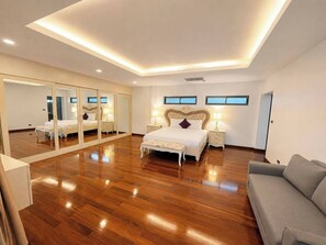 A spacious bedroom with a large mirror, a bed with a headboard, bedside tables with lamps, and a grey sofa. - Smith & Appy Seaview Penthouse (Koh Samui)