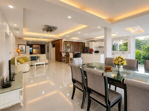 A modern living space with a dining area, kitchen, and a view of greenery. - Smith & Appy Seaview Penthouse (Koh Samui)