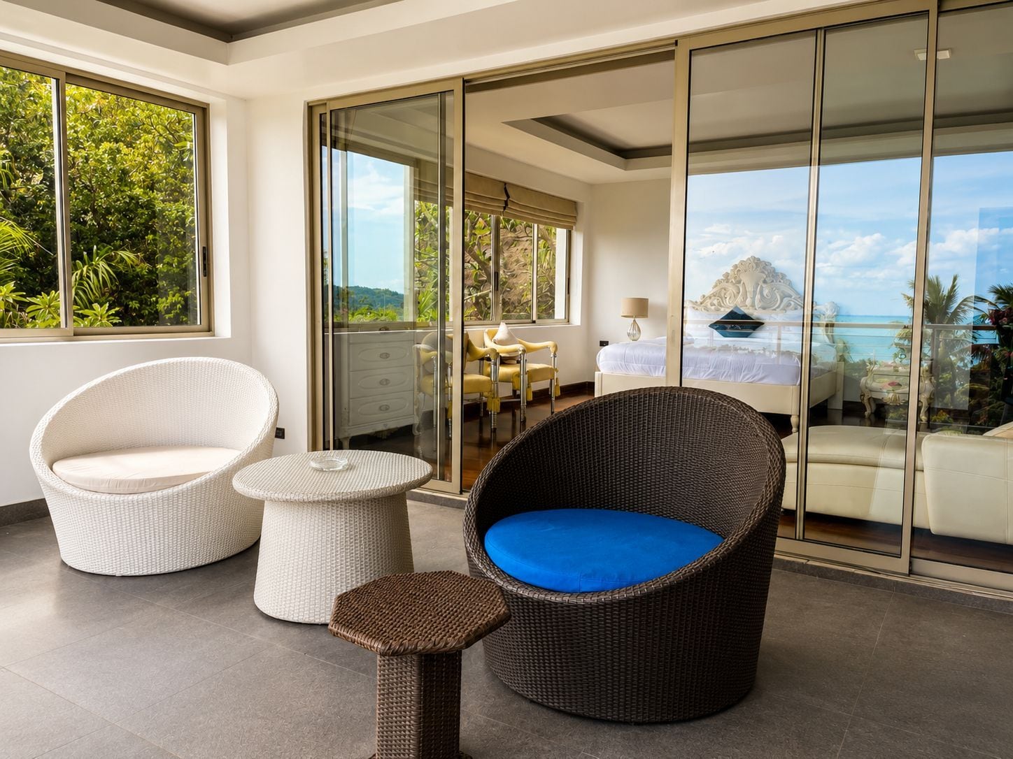 A balcony with wicker furniture, a view of the sea, and a glass door leading to a bedroom.