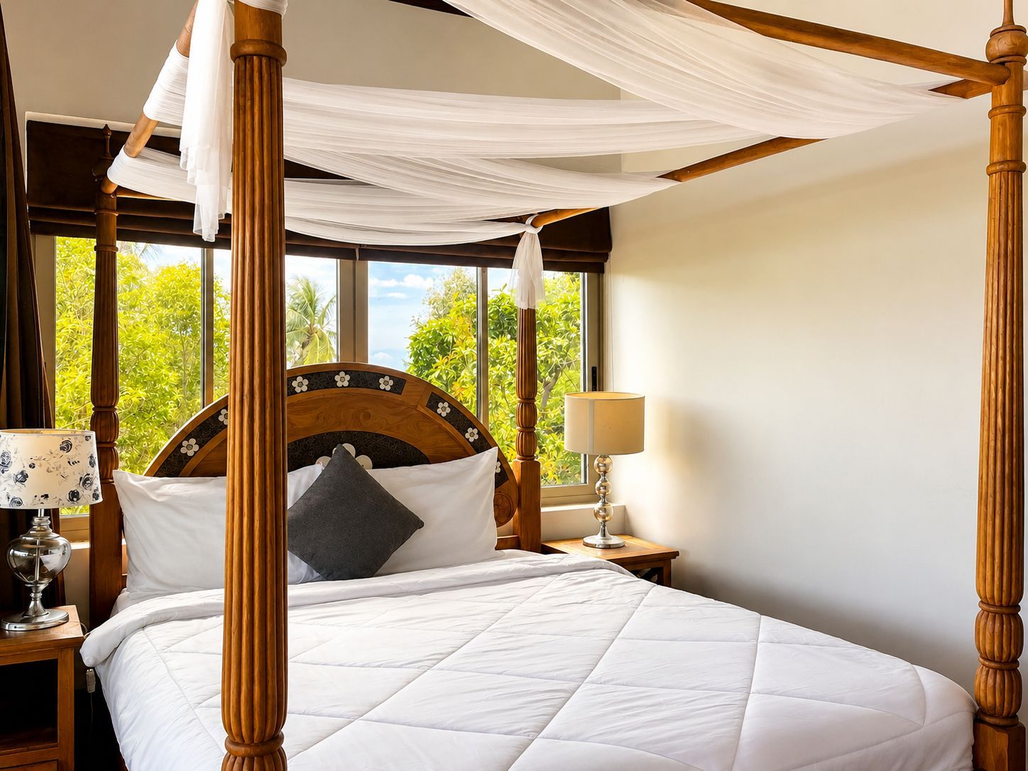 A four-poster bed with a canopy, a bedside table with a lamp, and a view of greenery outside.
