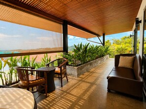 A covered outdoor seating area with a view of the ocean, wooden furniture, and potted plants. - Smith & Appy Luxury Seaview Penthouse (Koh Samui)