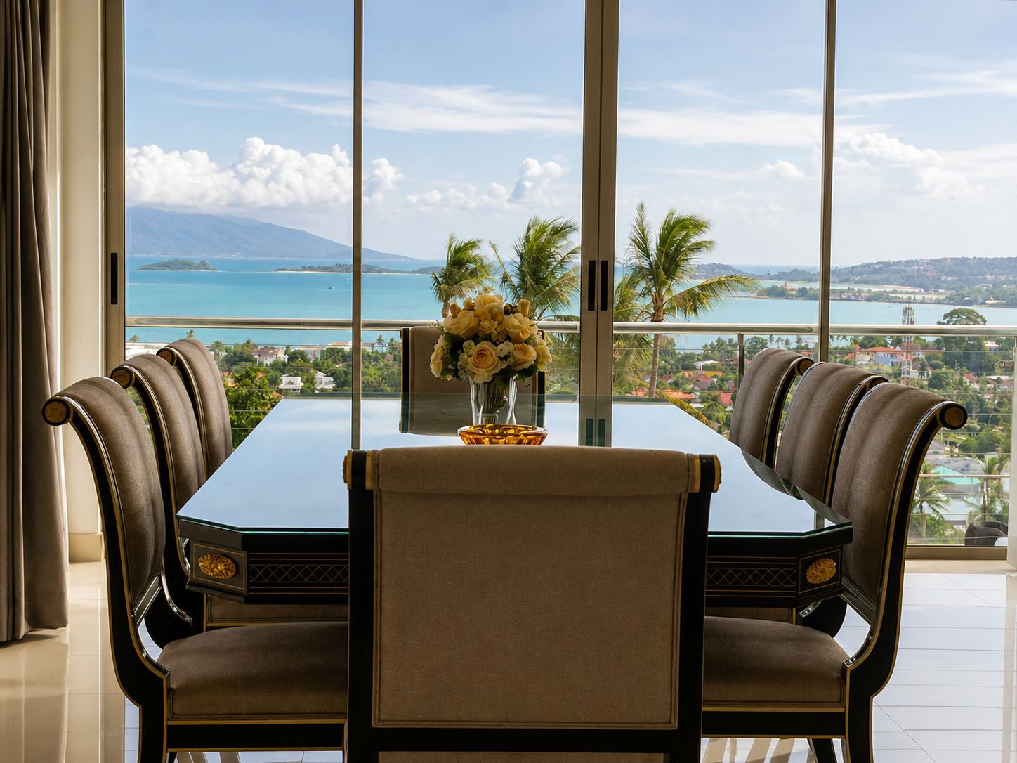 A dining area with a table and chairs, a vase of flowers, and a view of a coastal landscape.