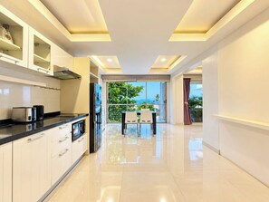A modern kitchen with a dining area, large windows, and a view of greenery. - Smith & Appy Luxury Seaview Penthouse (Koh Samui)