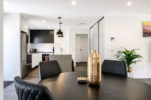 Eine moderne Küche mit dunklen Schränken, einem Edelstahlkühlschrank und einem Essbereich mit einem runden Tisch und schwarzen Stühlen.