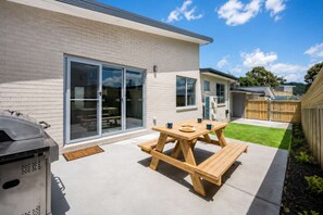 Een achtertuin met een terras, een barbecue en een schuifpui die leidt naar een overdekt terras.