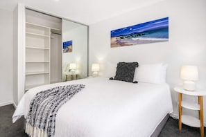Een hotelkamer met een bed, bedlampjes, een schilderij van een nachthemel, een kast en een klein tafeltje.