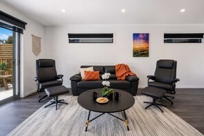 Ein modernes Wohnzimmer mit einer Couch, zwei Sesseln, einem Couchtisch und einem Gemälde an der Wand.