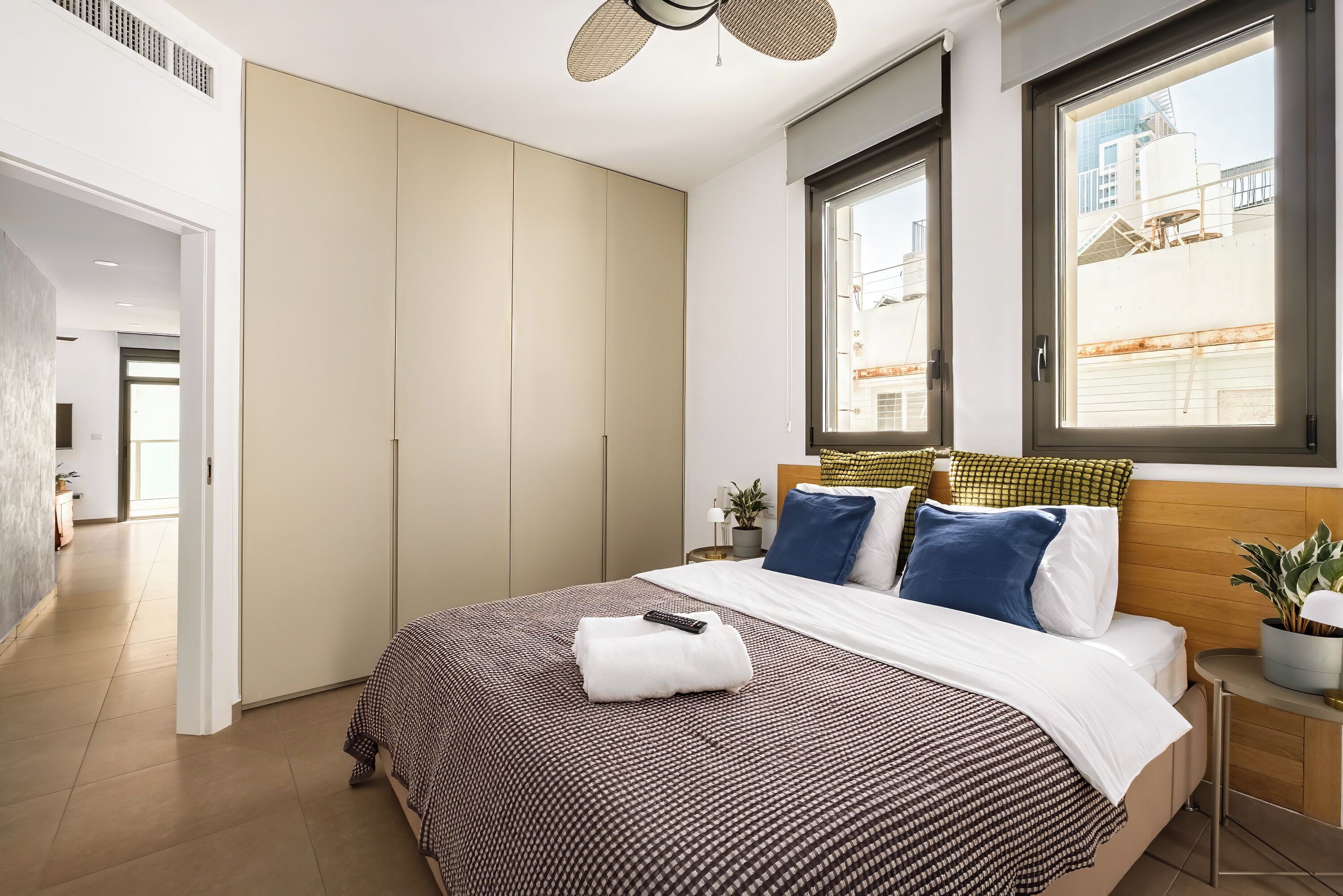A modern bedroom with a large bed, a wardrobe, and a window with a view of buildings.